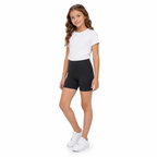 Niña usando calza corta de algodón negra, polera blanca y zapatillas blancas en pose lateral
