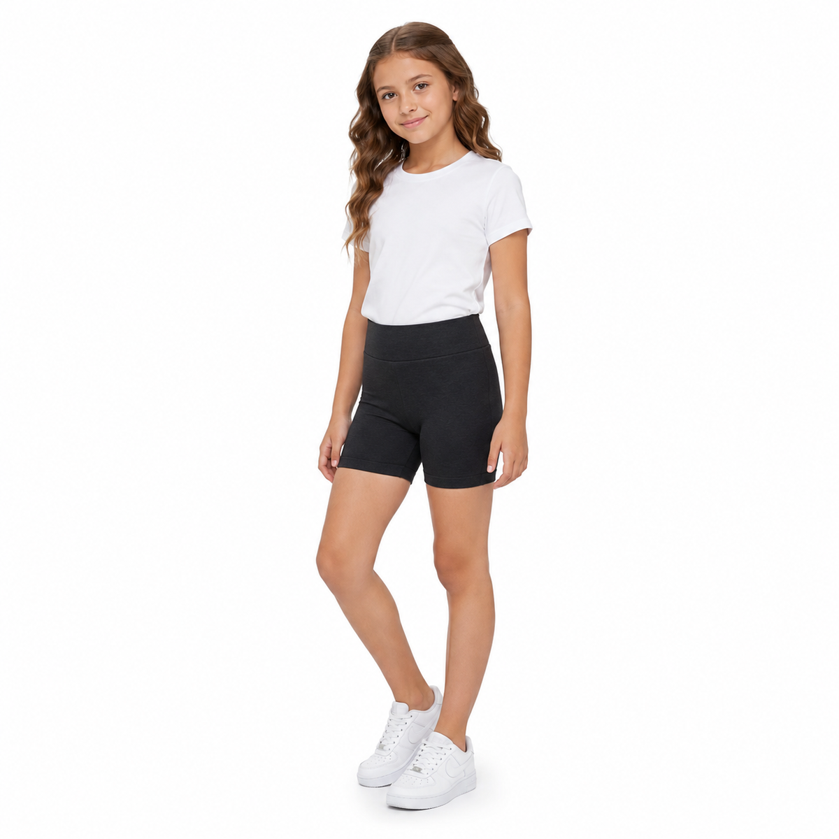 Niña usando calza corta de algodón negra, polera blanca y zapatillas blancas en pose lateral