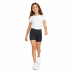 Niña caminando con calza corta escolar negra, polera blanca y zapatillas blancas sobre fondo blanco