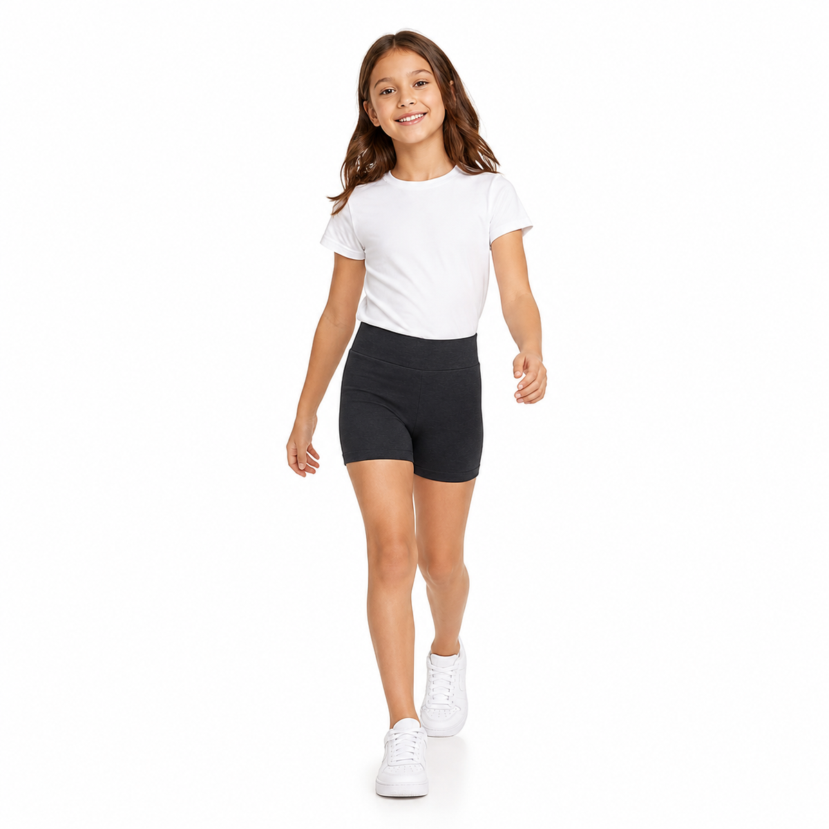 Niña caminando con calza corta escolar negra, polera blanca y zapatillas blancas sobre fondo blanco