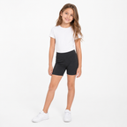 Niña con polera blanca, calza corta escolar negra y zapatillas blancas en vista frontal